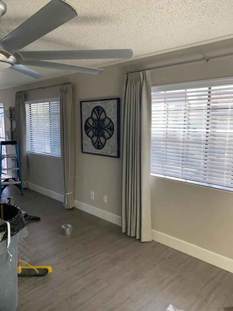 Pinch pleat drapery on decorative hardware beside wood blinds